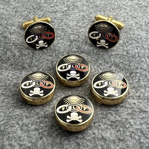 May include: Set of six gold-toned cufflinks and buttons featuring a black enamel design with a skull and crossbones, an eye, and the letters "FLIT" in a circle.