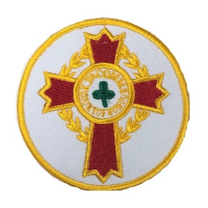 May include: A round, white embroidered patch with a red cross surrounded by a gold wreath. The cross has a smaller green cross in the center. The wreath has the words "The Order of St. John" in gold lettering.