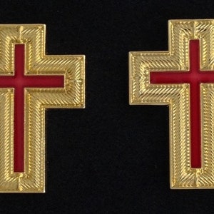 Può includere: Due croci dorate con centri in smalto rosso. Le croci hanno un design testurizzato e a motivi.