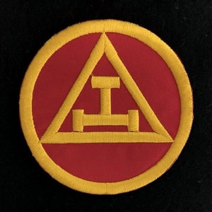 May include: A red and gold embroidered patch with a Masonic symbol. The symbol is a triangle with a T-shaped object inside.