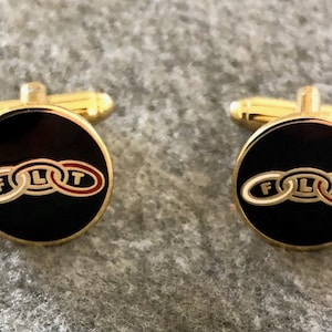 May include: A pair of gold cufflinks with black enamel and a white and red logo that says "FLIT" in a circle.
