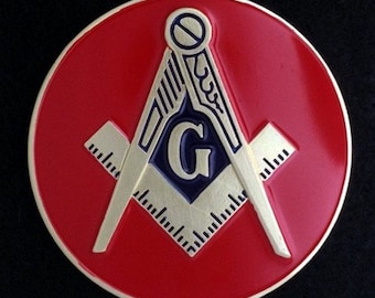 May include: A red circular car emblem with a gold Masonic symbol. The symbol features a compass and square with a 'G' in the center.