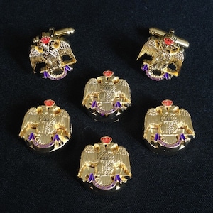 May include: Gold-toned cufflinks and lapel pins featuring a double-headed eagle design with a red crown and accents of purple and red. The lapel pins have the number "33" on them. The cufflinks have a gold bar closure.