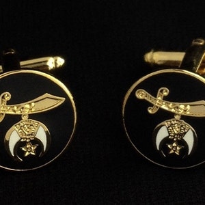 以下が含まれることがあります： 黒のエナメルを背景にした金色のカフスボタンのペア。カフスボタンには、金の三日月と星が描かれており、その上に金の三日月が描かれています。
