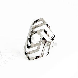 May include: A silver-colored ring with a geometric design. The ring features a series of angular, open spaces, creating a modern and architectural aesthetic. The ring is set against a white background, highlighting its metallic sheen. The jewelry piece is a statement accessory.