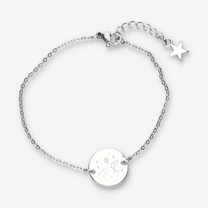 Peut inclure: Un bracelet en cha&icirc;ne argent avec un pendentif rond repr&eacute;sentant une constellation du zodiaque. Le pendentif a des symboles d'&eacute;toile, de soleil et de lune. Le bracelet a un fermoir &agrave; homard et un prolongement en forme d'&eacute;toile.