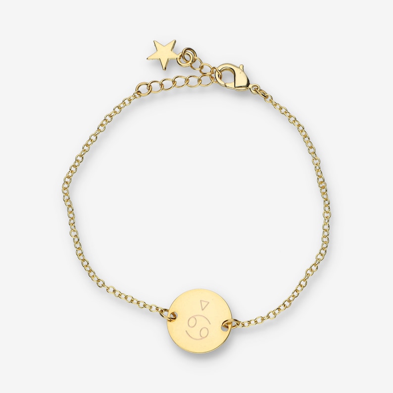 Peut inclure: Bracelet en cha&icirc;ne dor&eacute;e avec un petit charme en forme d'&eacute;toile et un charme rond grav&eacute; du symbole du zodiaque Cancer.