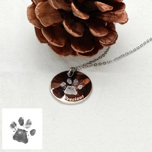 May include: Silver necklace with a round pendant featuring a paw print and the word "Precious" engraved on it. The pendant is hanging from a silver chain.