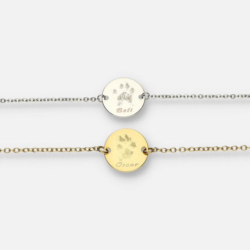 Puede incluir: Dos pulseras delicadas con colgantes circulares. Una es plateada, la otra dorada. Cada colgante presenta una huella de pata y un nombre: "Beti" y "Oscar". Las pulseras tienen un dise&ntilde;o de cadena fina, ideal para el uso diario.