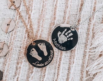 May include: Two gold and silver necklaces with round pendants. The gold pendant has a baby's footprint and the text "Louise 20.06.2021". The silver pendant has a baby's handprint and the text "Mathias".