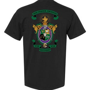 Pode incluir: T-shirt preto com um design de brasão com detalhes dourados, verdes, roxos e brancos. O brasão inclui uma cruz, balanças e espadas, com texto em latim. Uma t-shirt elegante.