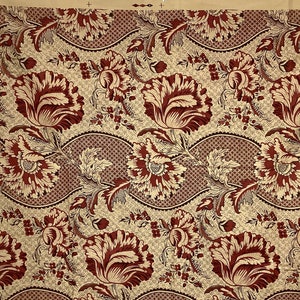 May include: A beige fabric with a repeating pattern of red stylized flowers and leaves. The fabric has a woven texture.