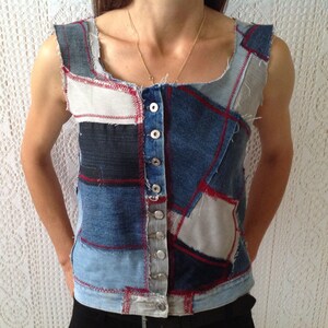 Könnte beinhalten: Eine ärmellose Jeansweste mit Patchwork-Design. Die Weste besteht aus verschiedenen Blautönen von Jeans und hat rote Nähte. Die Weste hat einen Knopfverschluss.