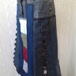 K&ouml;nnte beinhalten: Ein langer Jeansrock aus verschiedenen zusammengen&auml;hten Jeansst&uuml;cken. Der Rock hat eine dunkelblaue Jeansbasis mit einem hellblauen Jeanspanel an der Seite. Der Rock hat eine Reihe von Metallschnallen an der Seite.