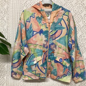 Puede incluir: Chaqueta con capucha colorida con un estampado floral y geométrico en tonos pastel de rosa, azul, verde y melocotón. La chaqueta tiene cremallera frontal, bolsillos y cintura ajustable. Fabricada en material ligero.