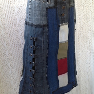 K&ouml;nnte beinhalten: Ein Jeansrock mit Patchwork-Design. Der Rock besteht aus verschiedenen Blaut&ouml;nen von Jeans und hat einen roten, wei&szlig;en und gr&uuml;nen Streifen auf der rechten Seite. Der Rock hat eine Reihe von Metallschnallen auf der linken Seite.