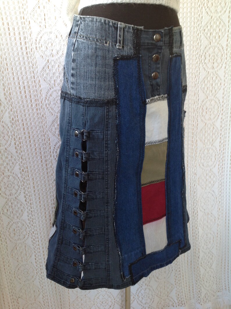 K&ouml;nnte beinhalten: Ein Jeansrock mit Patchwork-Design. Der Rock besteht aus verschiedenen Blaut&ouml;nen von Jeans und hat einen roten, wei&szlig;en und gr&uuml;nen Streifen auf der rechten Seite. Der Rock hat eine Reihe von Metallschnallen auf der linken Seite.