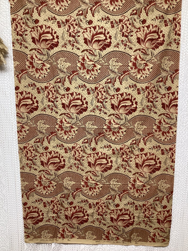May include: Red and gold floral fabric with a repeating pattern of stylized flowers and leaves. The fabric has a textured, woven look.