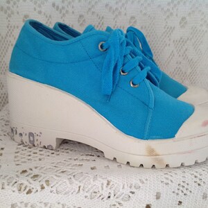 Peut inclure: Une paire de baskets compensées en toile bleue avec des semelles blanches. Les baskets ont une fermeture à lacets et une pointe arrondie.