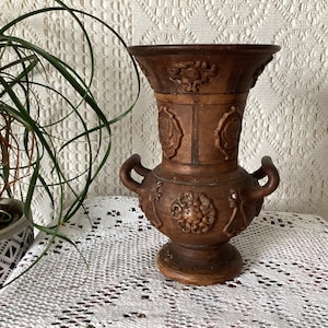May include: A brown ceramic vase with intricate carvings and two handles. The vase has a wide mouth and a narrow base.