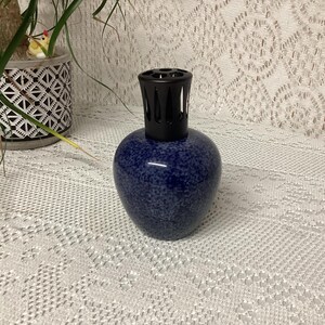 May include: A dark blue speckled ceramic essential oil diffuser with a black top. The diffuser has a rounded body and a textured surface. The diffuser is a decorative item for aromatherapy and home fragrance.