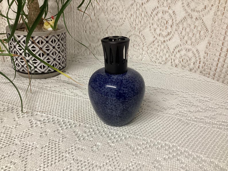 May include: A dark blue speckled ceramic essential oil diffuser with a black top. The diffuser has a rounded body and a textured surface. The diffuser is a decorative item for aromatherapy and home fragrance.