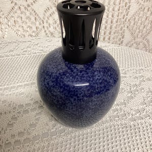 May include: A blue speckled ceramic fragrance lamp with a black metal top. The lamp has a rounded shape and a glossy finish. The top has a decorative design with vertical slits.