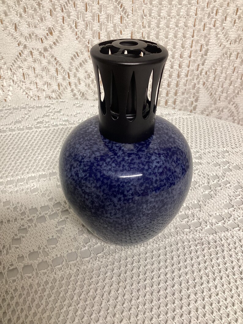 May include: A blue speckled ceramic fragrance lamp with a black metal top. The lamp has a rounded shape and a glossy finish. The top has a decorative design with vertical slits.