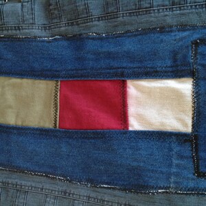 K&ouml;nnte beinhalten: Nahaufnahme einer Jeansjacke mit Patchwork-Design. Der Patch besteht aus vier verschiedenen Stoffen: Wei&szlig;, Gr&uuml;n, Rot und Beige. Die Patches sind mit schwarzem Faden zusammengen&auml;ht.