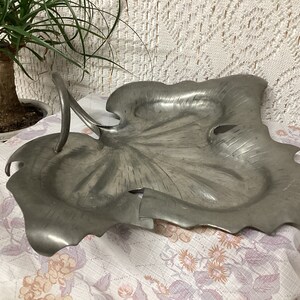 May include: A silver leaf-shaped serving dish with a handle. The dish is made of pewter and has a textured surface.