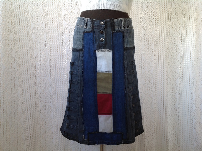 K&ouml;nnte beinhalten: Ein Jeansrock mit Patchwork-Design. Der Rock besteht aus verschiedenen Blaut&ouml;nen von Jeans und hat ein rotes, wei&szlig;es und gr&uuml;nes Panel in der Mitte.