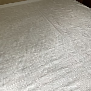 May include: White bedspread with a quilted pattern. The pattern is composed of squares with various textures, including dots and floral designs. The bedspread covers the entire bed, creating a clean and classic look.