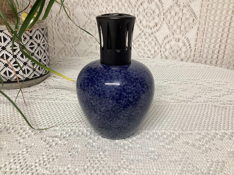 May include: A blue speckled ceramic fragrance lamp with a black top. The lamp has a rounded body and a decorative design. The lamp is a home decor item.
