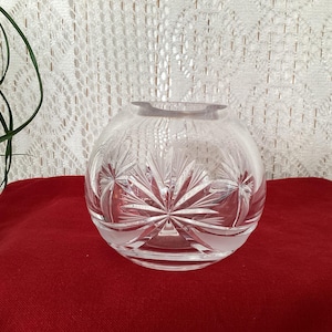 May include: A clear glass vase with a cut-glass design. The vase has a round shape and a wide opening.