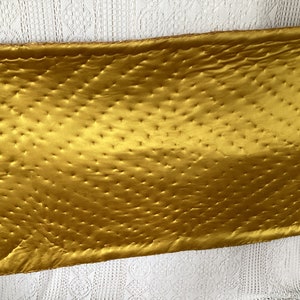 May include: A gold quilted fabric with a diamond pattern. The fabric is smooth and shiny.
