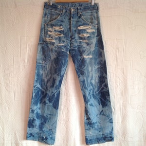 Könnte beinhalten: Blaue Jeans aus Denim mit Used-Look, Batik-Muster und mehreren Rissen und Löchern.