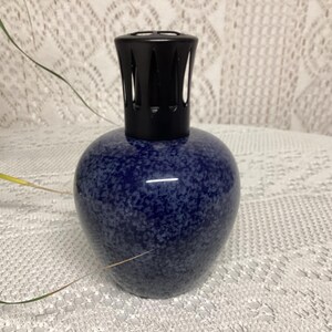 May include: A blue speckled ceramic essential oil diffuser with a black top. The diffuser has a rounded base and a cylindrical top with vertical slits. The speckled pattern gives the diffuser a unique look.