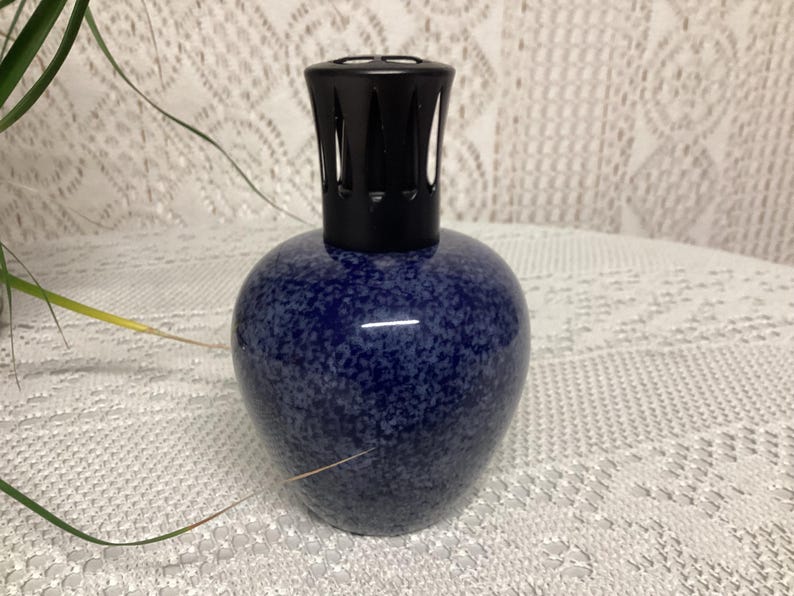 May include: A blue speckled ceramic essential oil diffuser with a black top. The diffuser has a rounded base and a cylindrical top with vertical slits. The speckled pattern gives the diffuser a unique look.