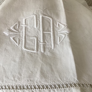 May include: White linen tablecloth with a delicate embroidered monogram of the letters "GA" in a diamond shape.