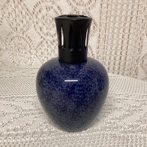 May include: A blue speckled ceramic fragrance lamp with a black top. The lamp has a rounded body and a cylindrical top with vertical slits. The lamp is designed to diffuse essential oils and add a decorative touch to any room.