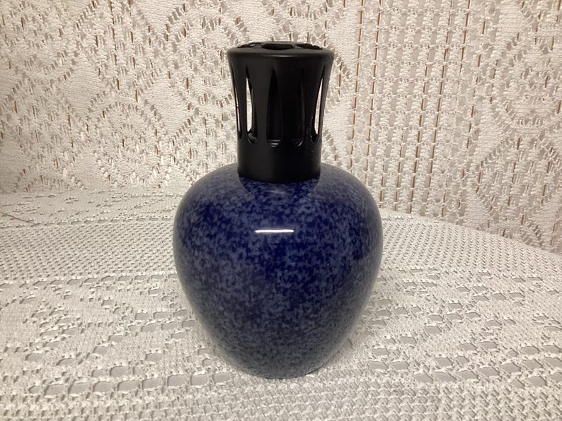 May include: A blue speckled ceramic fragrance lamp with a black top. The lamp has a rounded body and a cylindrical top with vertical slits. The lamp is designed to diffuse essential oils and add a decorative touch to any room.