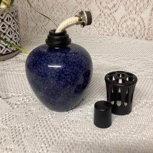 May include: A navy blue speckled ceramic oil lamp with a white wick and black accents. Includes a black metal cap and a small black cap. The lamp is designed for aromatherapy or decorative purposes.