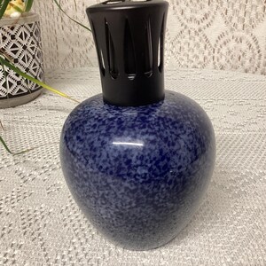 May include: A blue speckled ceramic fragrance lamp with a black top. The lamp has a rounded body and a textured surface. The black top has a slotted design. The lamp is a decorative item.
