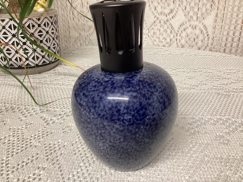 May include: A blue speckled ceramic fragrance lamp with a black top. The lamp has a rounded body and a textured surface. The black top has a slotted design. The lamp is a decorative item.