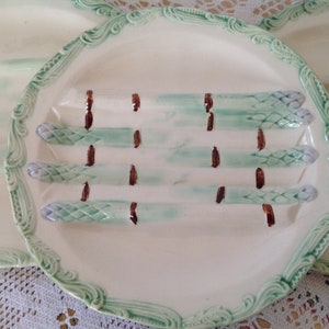 Puede incluir: Un juego de tres platos de servir de cerámica blanca con ribetes verdes y marrones. Cada plato presenta un diseño de tallos de espárragos.