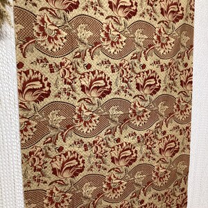 May include: Red and gold floral fabric with a repeating pattern of stylized flowers and leaves. The fabric has a textured, woven look.