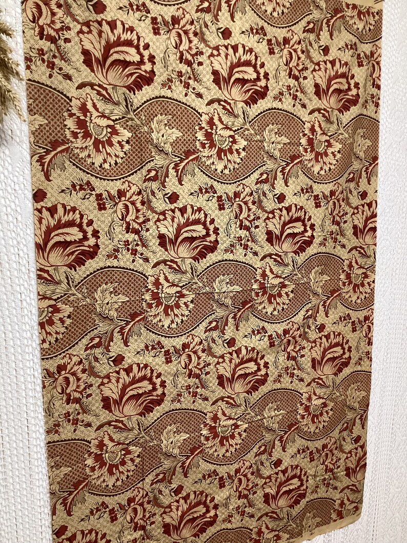 May include: Red and gold floral fabric with a repeating pattern of stylized flowers and leaves. The fabric has a textured, woven look.