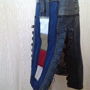 K&ouml;nnte beinhalten: Ein Jeansrock mit Patchwork-Design aus verschiedenen Stoffen in den Farben Blau, Rot, Wei&szlig; und Gr&uuml;n. Der Rock hat einen seitlichen Rei&szlig;verschluss und mehrere Metallringe entlang der Seitennaht.