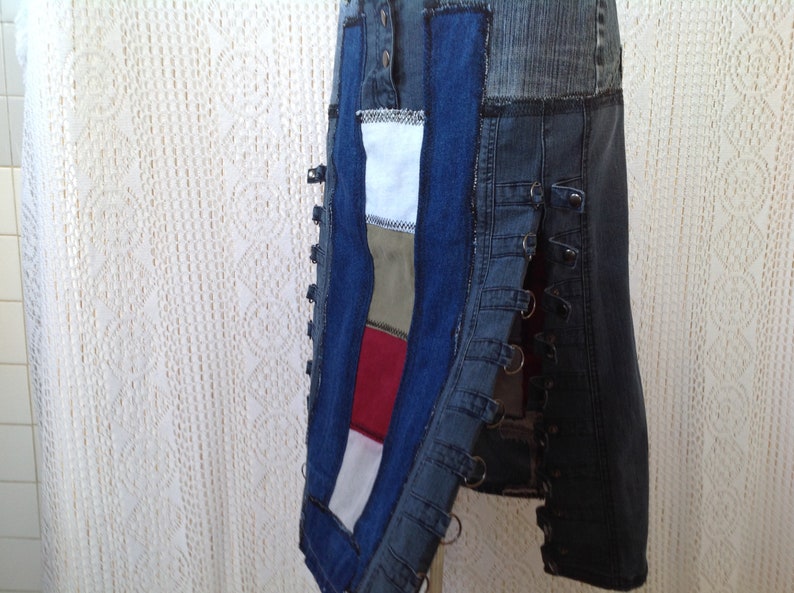 K&ouml;nnte beinhalten: Ein Jeansrock mit Patchwork-Design aus verschiedenen Stoffen in den Farben Blau, Rot, Wei&szlig; und Gr&uuml;n. Der Rock hat einen seitlichen Rei&szlig;verschluss und mehrere Metallringe entlang der Seitennaht.