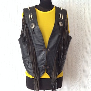 Peut inclure: Gilet en cuir noir avec des détails en franges et des boutons conchos argentés. Le gilet a un col à franges et un sous-pull jaune.